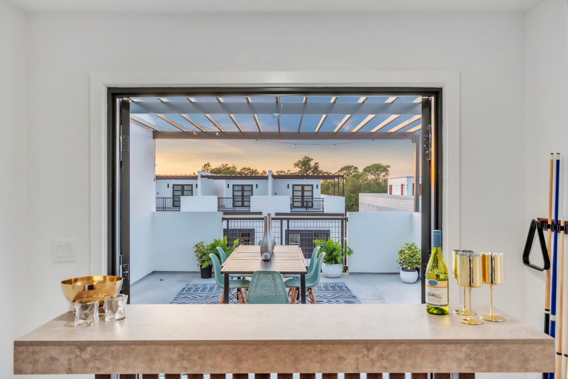 View from the loft bar through open doors to a rooftop dining table and the treetops of Pinellas Park at dusk