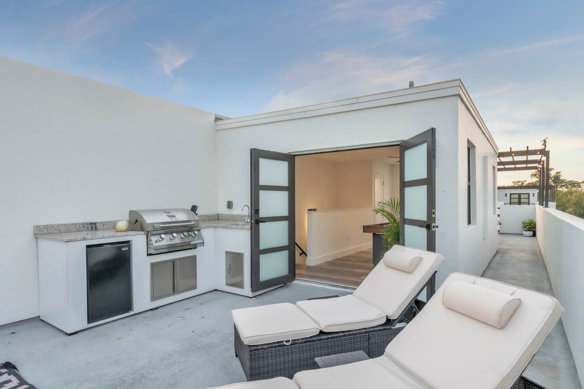 Rooftop outdoor kitchen with built-in grill beside loungers and open loft doors at Latitudes in the Park, Pinellas Park FL